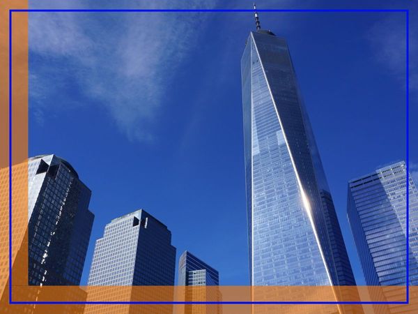 A low-angle view of modern glass skyscrapers in Manhattan against a bright blue sky.