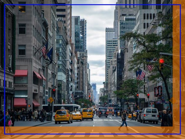 A busy street scene in Manhattan with yellow taxis, pedestrians, and tall buildings under a cloudy sky.