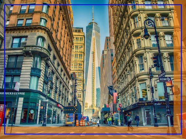 A street view in Manhattan looking towards One World Trade Center, surrounded by classic and modern buildings.